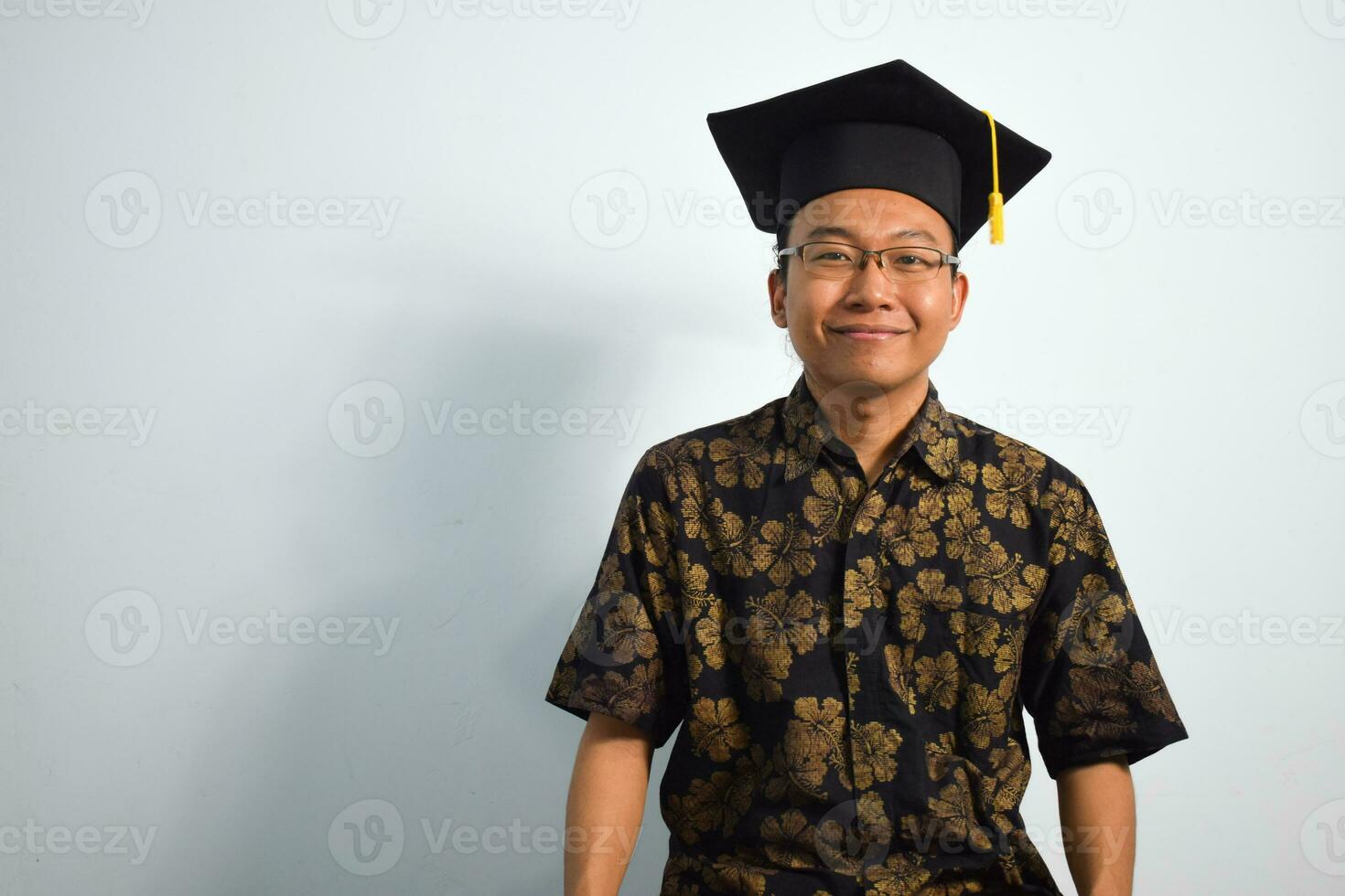 expresivo de adulto Indonesia masculino vestir batik, toga taza o graduación sombrero y los anteojos aislado en blanco fondo, expresiones de retrato graduación foto