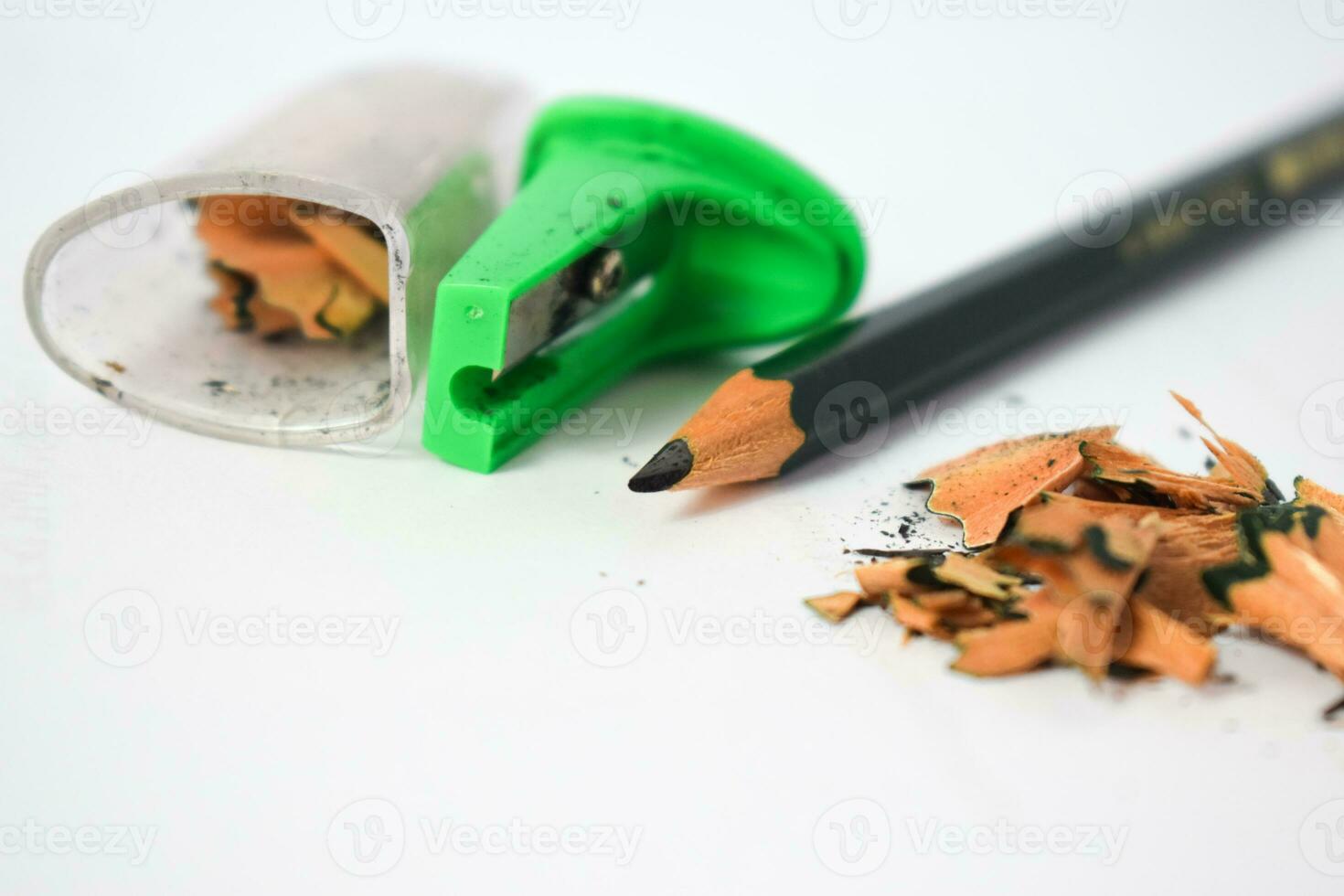 green pencil sharpener and dark green pencils, pencil shavings on white background photo