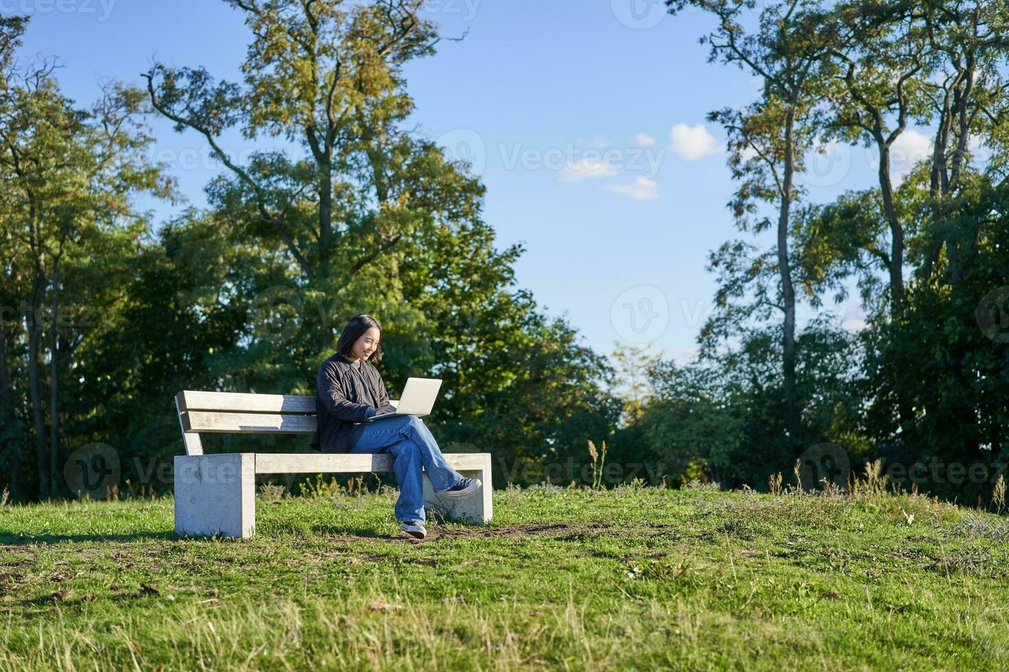 Portrait of young student, girl using laptop, sitting in park on bench, typing on computer photo