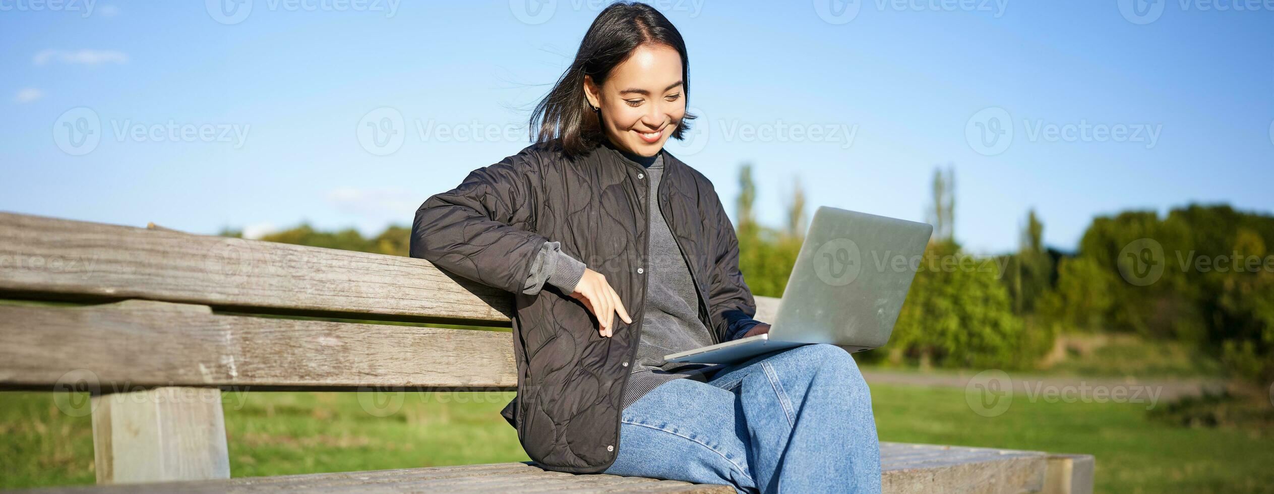 Portrait of smiling woman sitting with laptop, working on project or studying remotely, enjoying being in park photo