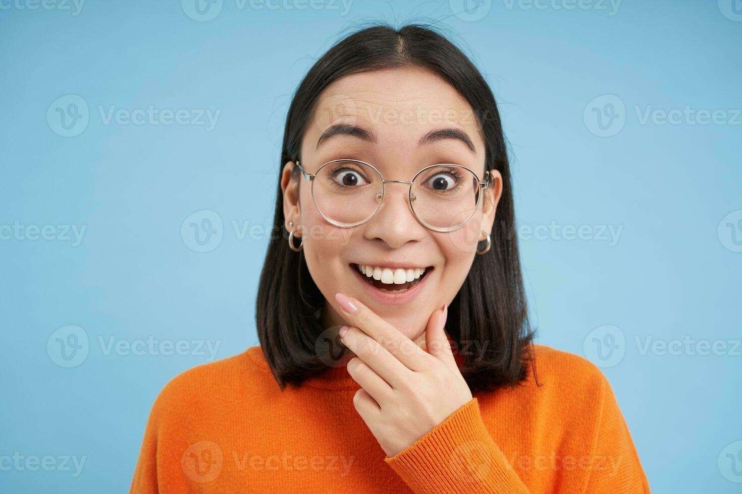 Portrait of smiling beautiful woman in glasses, testing her eyesight, wearing new spectacles, standing over blue background photo