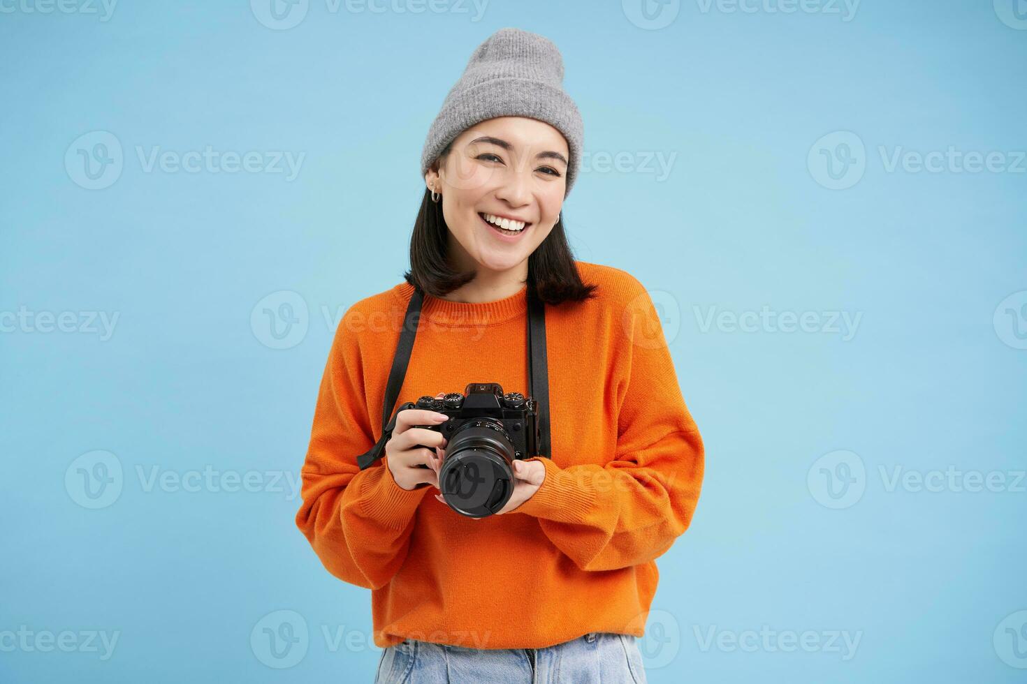 Stylish asian girl with digital camera, taking pictures. Woman photographer smiling, standing over blue background photo
