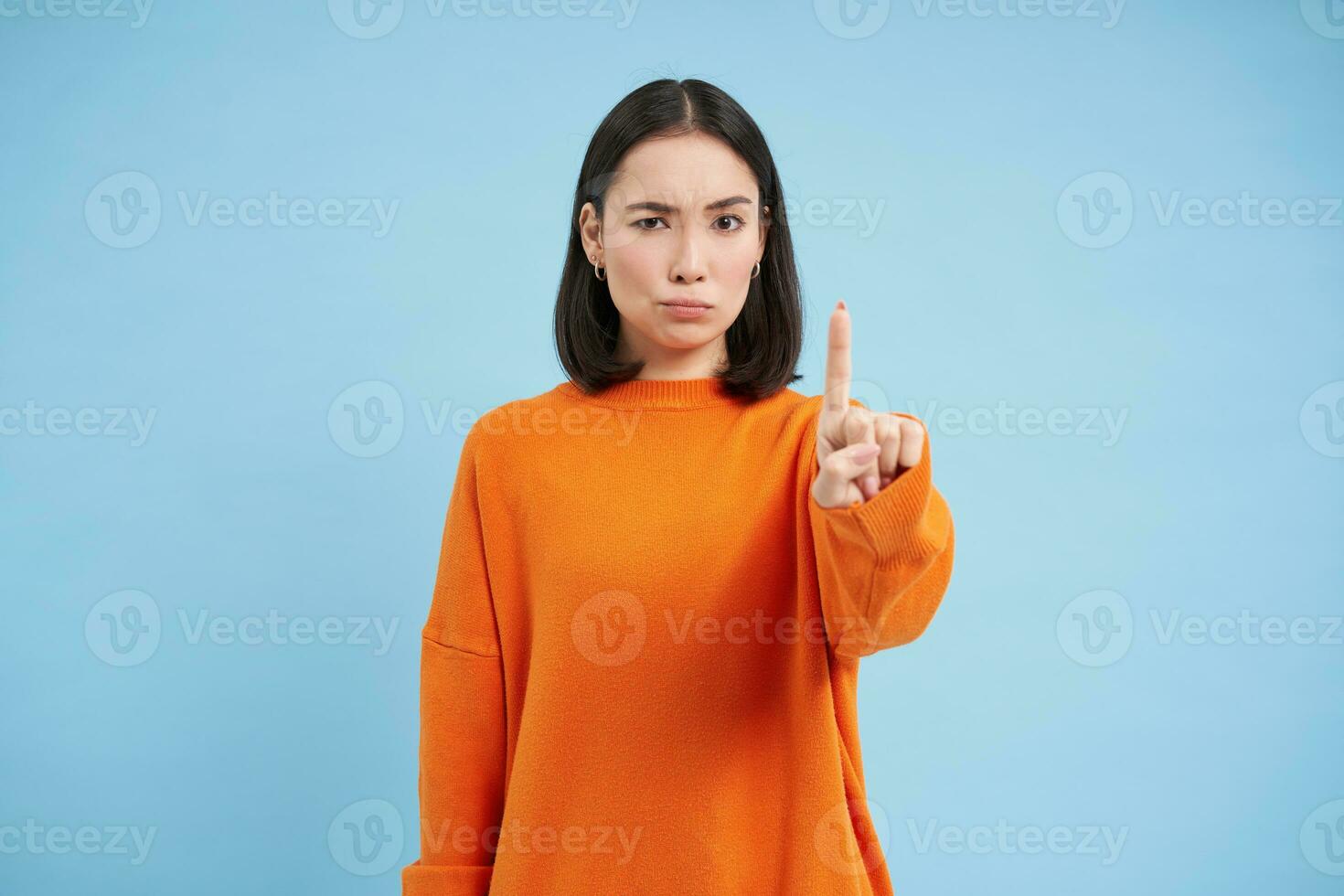 regla número uno. grave coreano niña muestra dedo, batidos dedo índice, desaprueba algo, prohíbe, soportes terminado azul antecedentes foto