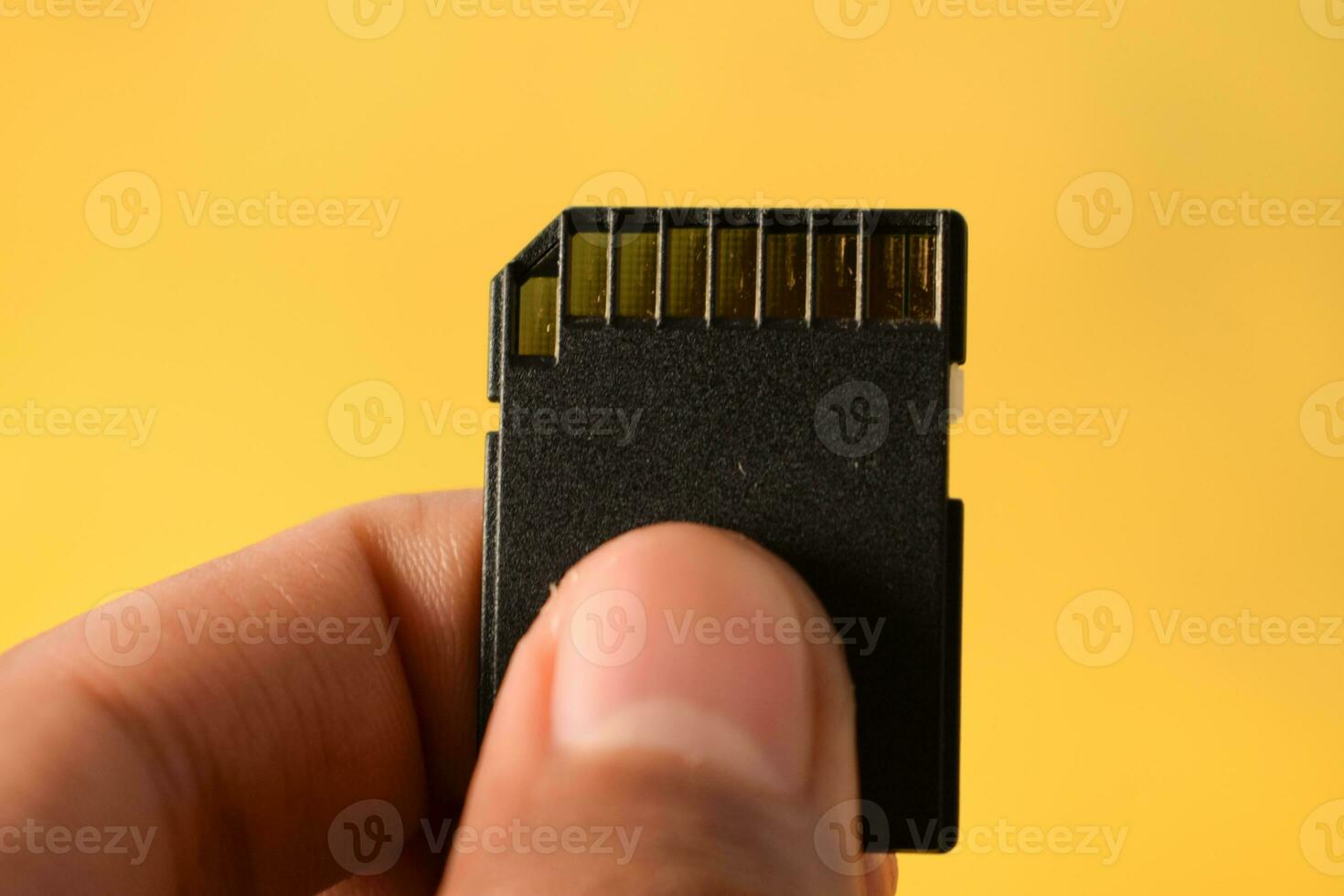 Close up hand holds SD Card for DSLR or Mirrorless camera on yellow background photo