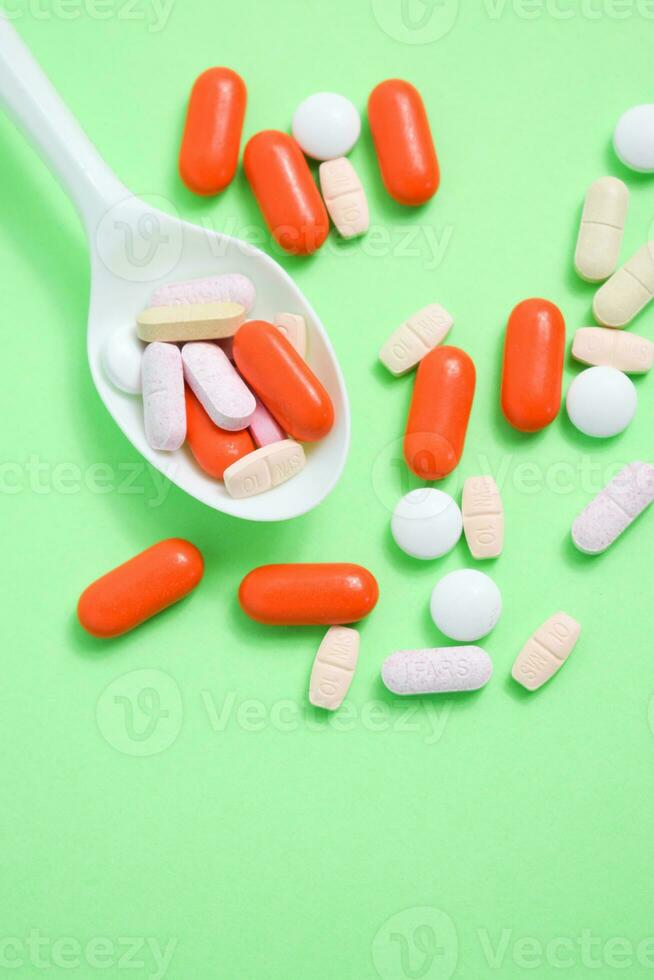 White spoon with colorful medical pills on green background, copy space photo