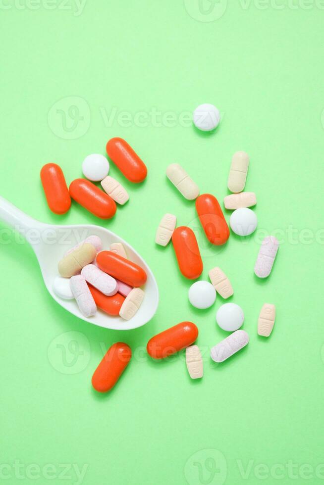 White spoon with colorful medical pills on green background, copy space photo