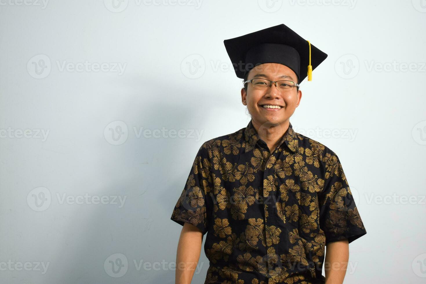 expresivo de adulto Indonesia masculino vestir batik, toga taza o graduación sombrero y los anteojos aislado en blanco fondo, expresiones de retrato graduación foto