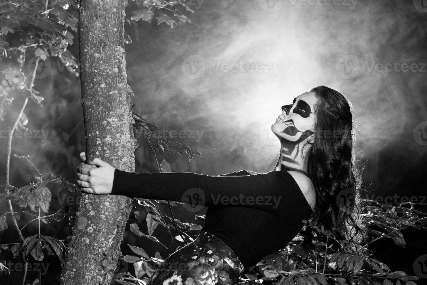 Portrait of young woman with scared halloween makeup in forrest. halloween make up sugar skull beautiful model with perfect hairstyle. Devil girl concept. photo