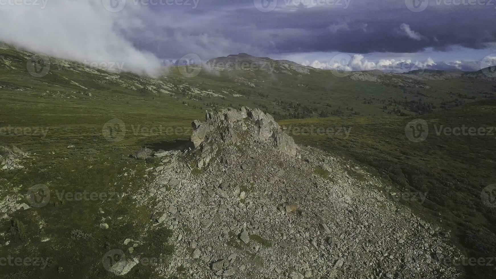 aéreo ver en verde prado con solitario rock y nublado cielo antecedentes. increíble montañas paisaje con grande rock a el medio de el césped. aéreo Disparo de montaña lado foto