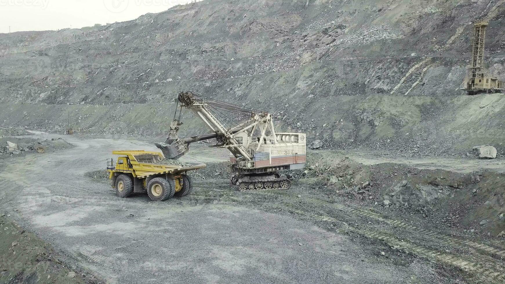 excavador y tugurio camión mientras cargando Roca mineral en un gris cantera, minería industria. existencias. pesado minería excavador cargas rock mineral dentro un cuerpo volcado grande minería camión, cantera equipo. foto