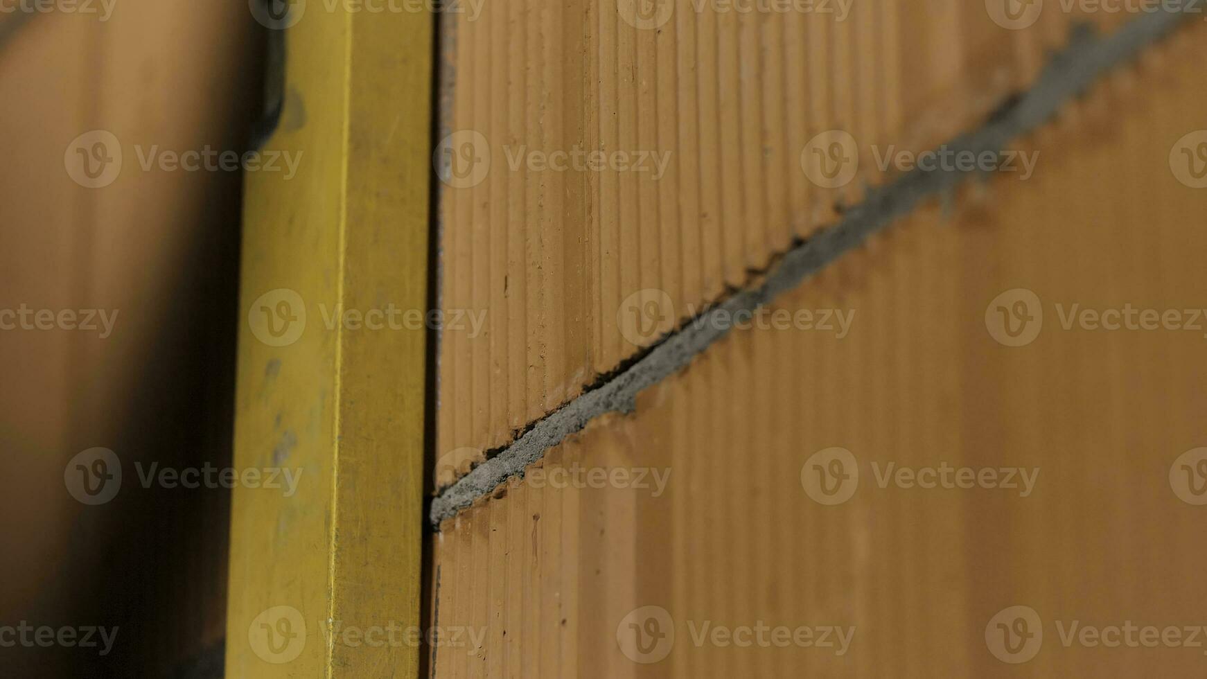 Bricklayer using a spirit level to check the wall and to draw a line with a pencil. Stock footage. Close up of man hands in protective gloves working with professional tool. photo