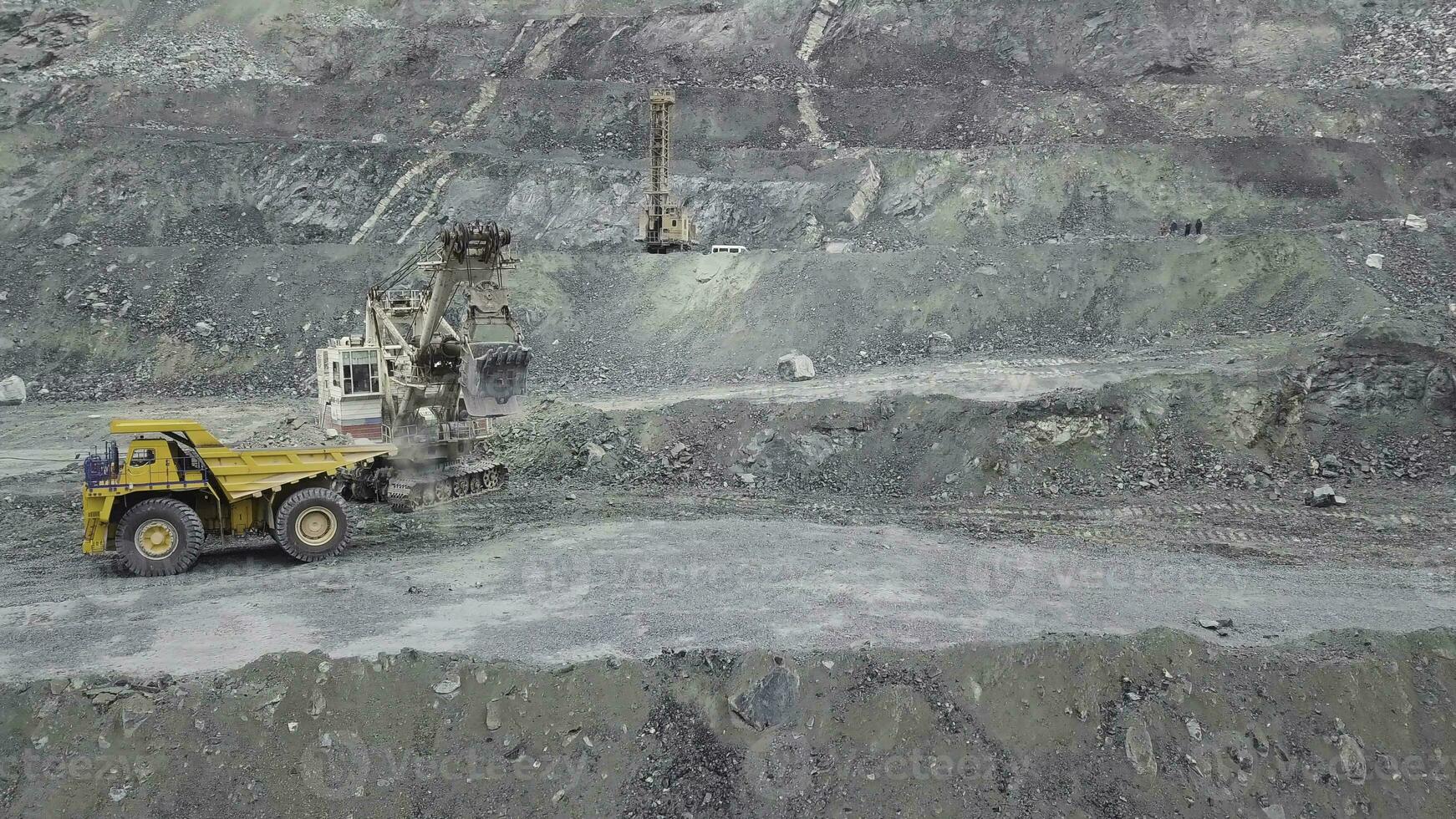 Excavator and dump truck while loading stone ore in a grey quarry, mining industry. Stock. Heavy mining excavator loads rock ore into a dump-body large mining truck, quarry equipment. photo