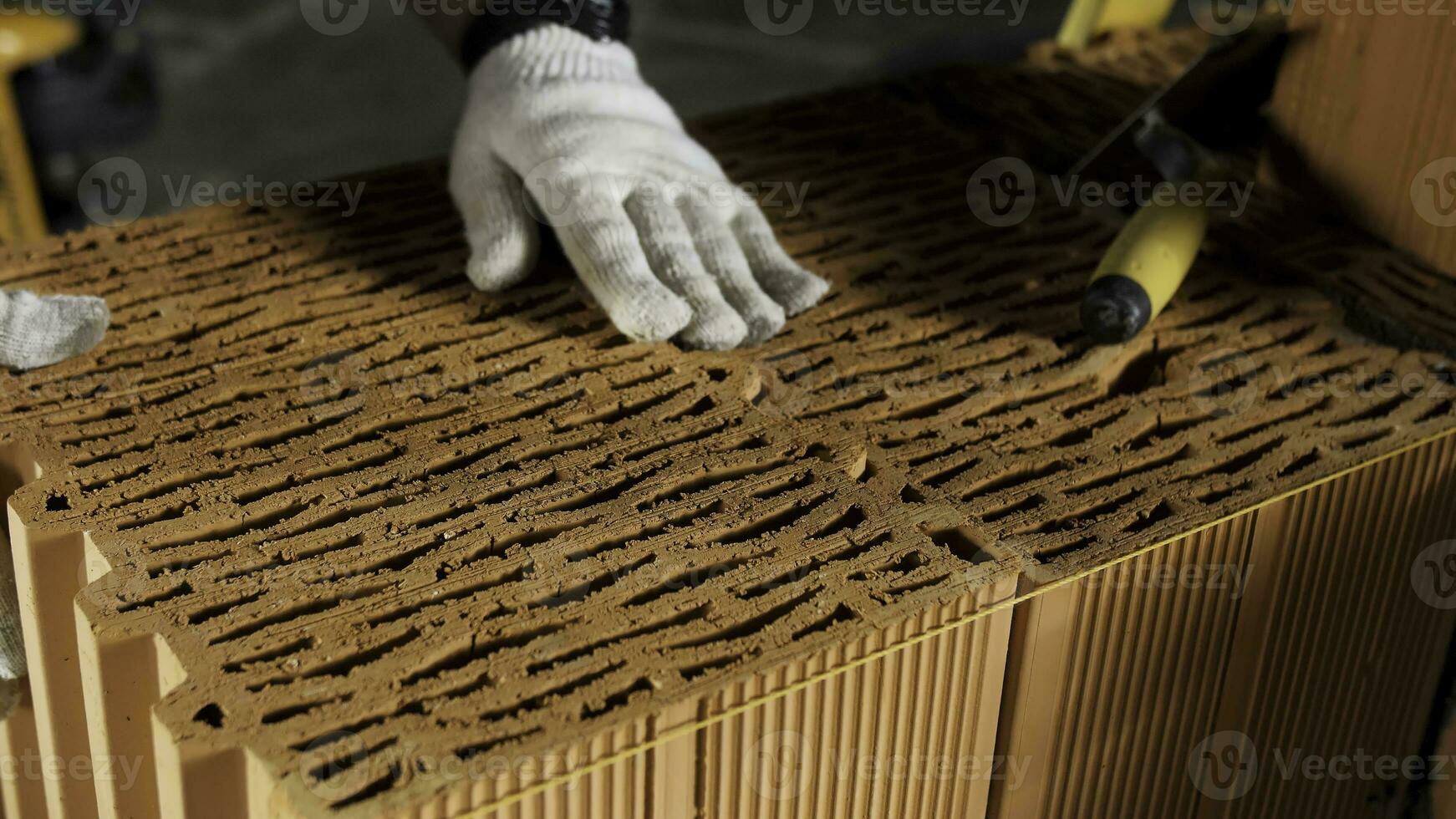 Industrial bricklayer worker placing bricks on cement while building walls. Stock footage. Close up of a man in protective gloves putting heavy brick block to form a layer. photo