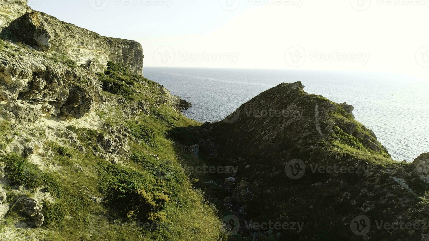 Peaceful blue sea and fresh green grass of a rocky slope at the coast. Shot. Magic path to the endless sea with clear blue sky on the background. photo