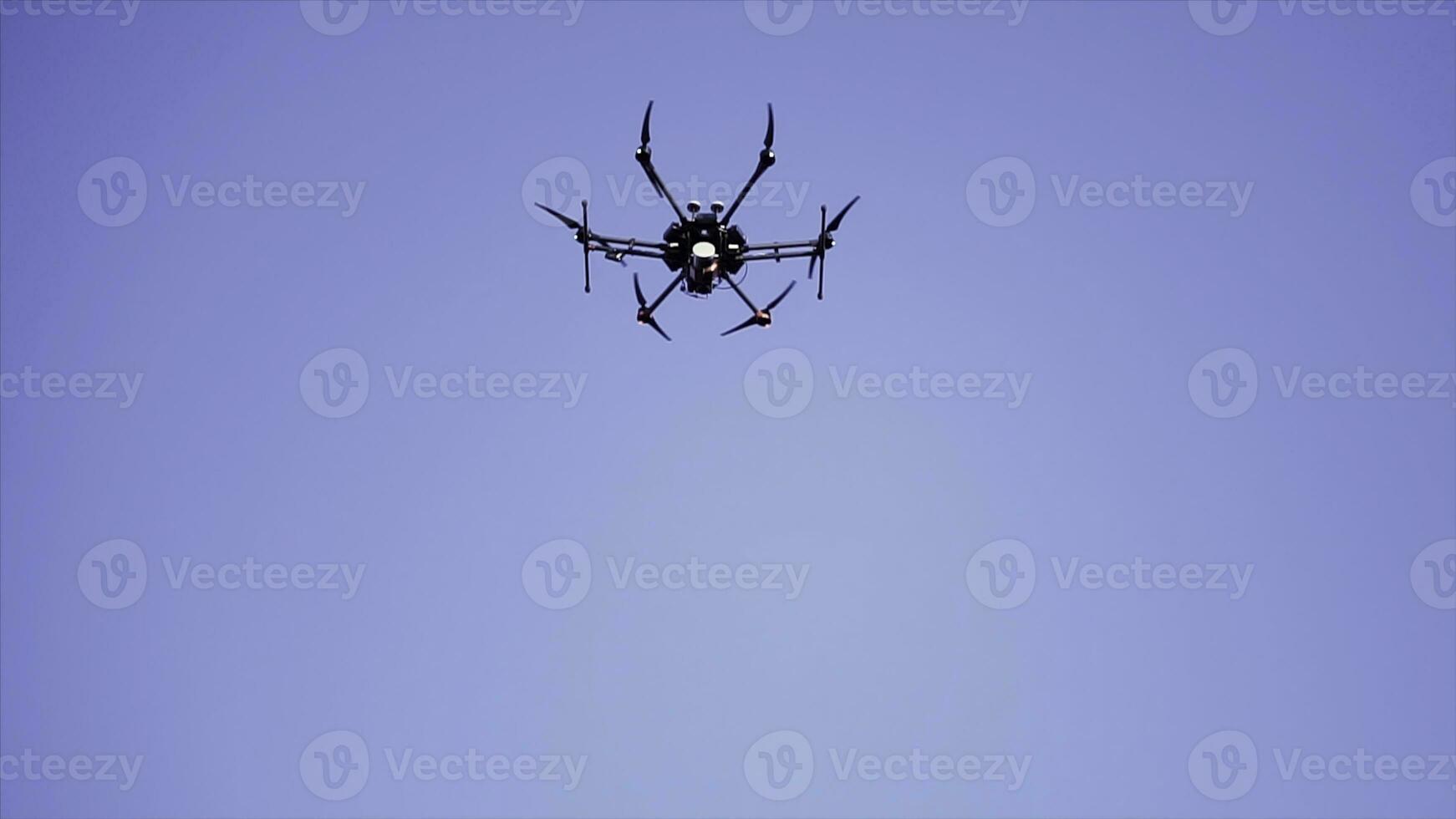 Black drone flying against the blue sky with spinning blades, bottom view. Clip. Compact quadcopter controlled by wireless remote shooting video footages and photos. photo