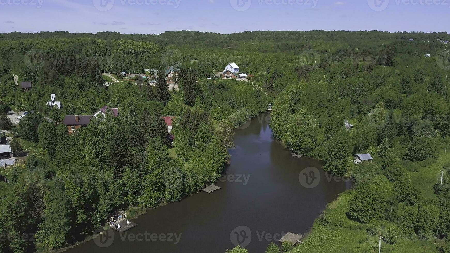 Aerial view of a town with many green trees located along the river in a sunny summer day. Clip. Ecologically clean area with small beautiful houses and narrow river. photo