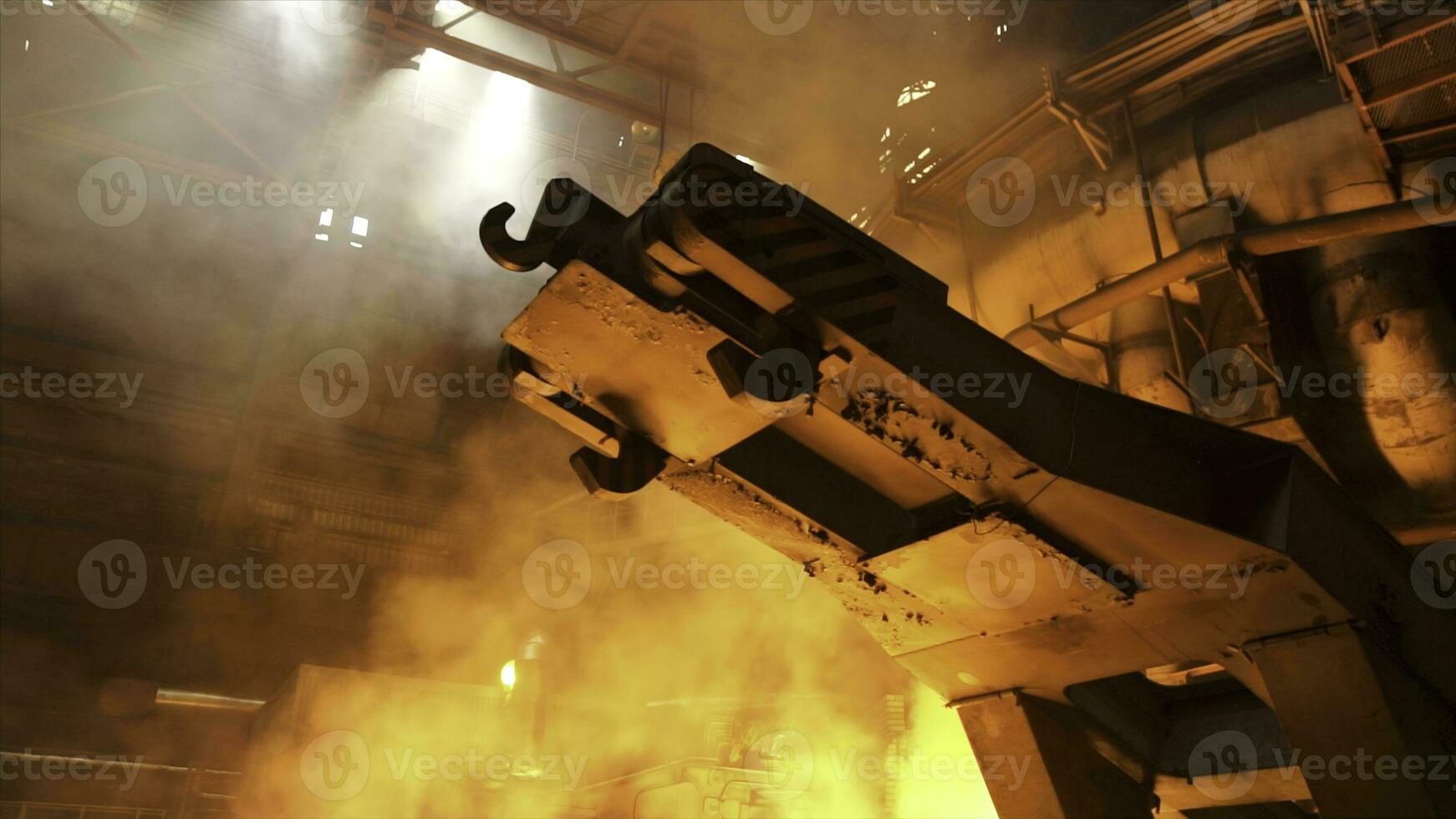 A mechanism with hooks in the hot shop with rising smoke and burning fire at the metallurgical plant. Stock footage. Heavy industry, equipment at the steel factory. photo