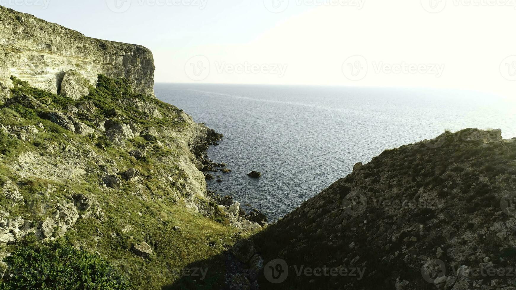 Spectacular view of steep dliffs at the ocean, Ireland. Shot. Green slope near calm water and the endless horizon on clear blue sky background. photo