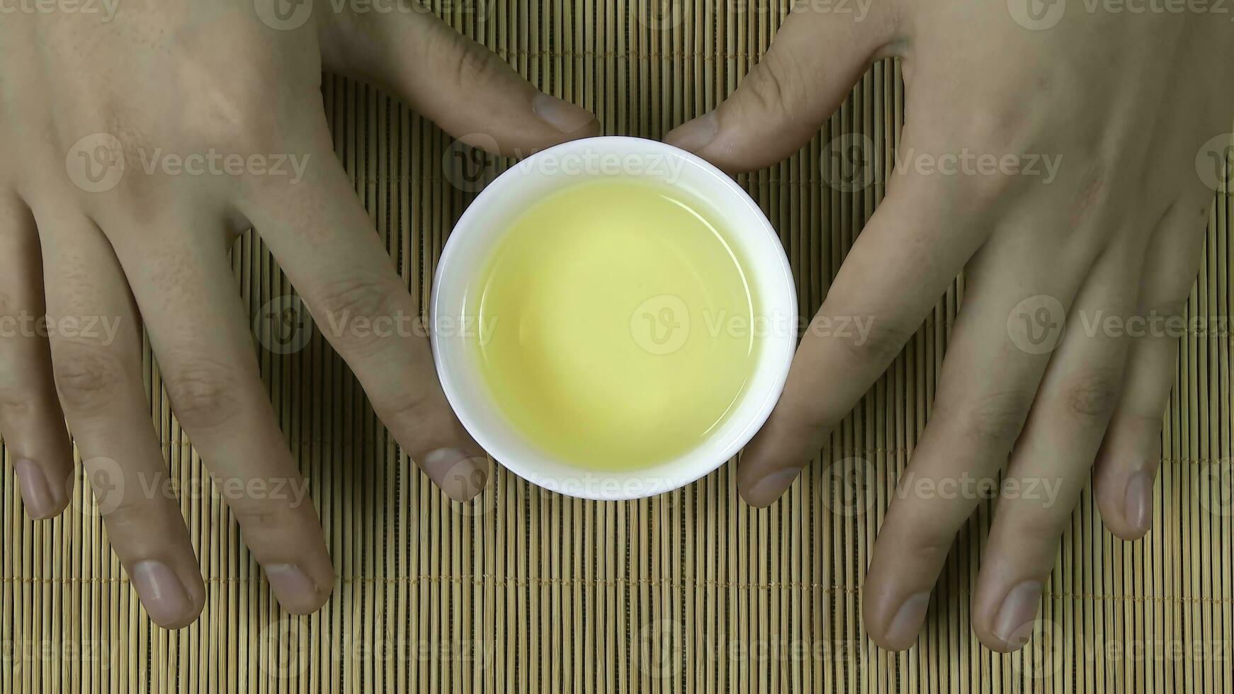 mujer manos participación blanco taza de chino té bambú fondo, parte superior vista. un mujer participación un taza de té. verde japonés sencha té en flores jarra foto