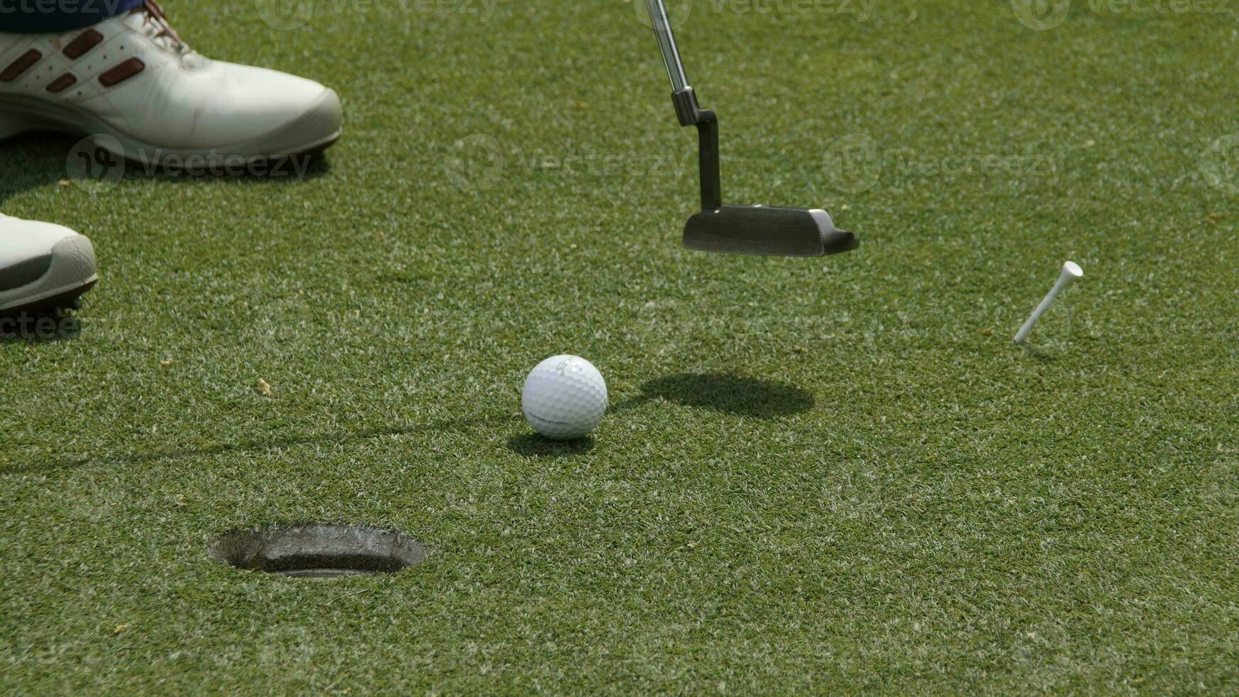 Professional golfer putting ball into the hole. Golf ball by the edge of hole with player in background on a sunny day. photo