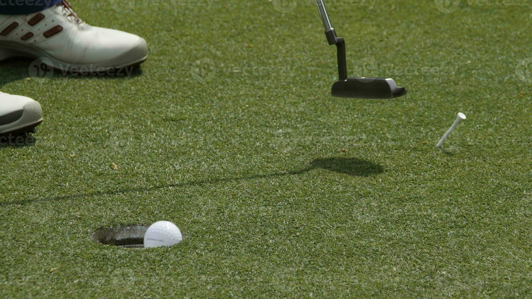 Professional golfer putting ball into the hole. Golf ball by the edge of hole with player in background on a sunny day. photo