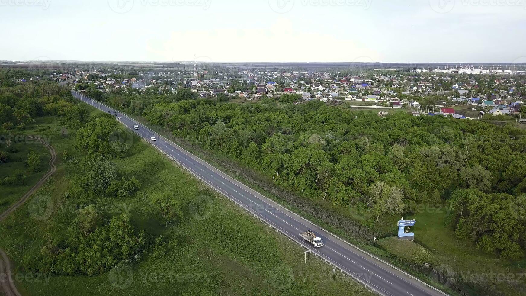 Top view of highway passing through village with forest. Clip. Track with passing cars on background of village with green forest and horizon with sky photo