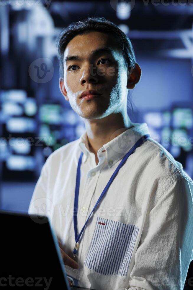 Computer scientist in data center uses laptop to prevent system overload during peak traffic periods. Licensed expert in server room ensuring enough network bandwidth for smooth operations photo