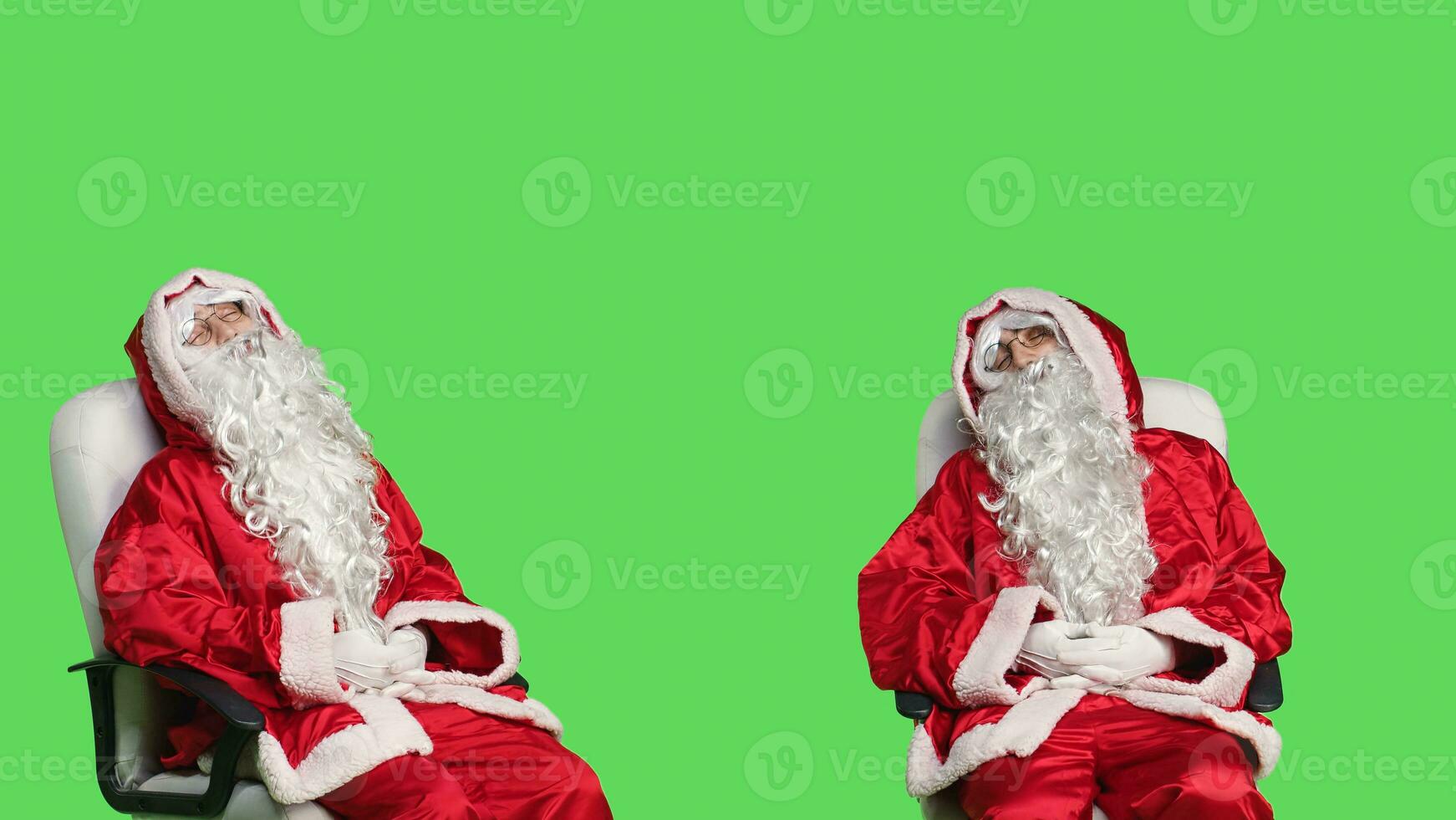 Father christmas falling asleep on chair, trying to keep eyes open in studio with greenscreen. Man in saint nick costume sleeping on camera, feeling tired and relaxing before festive celebration. photo