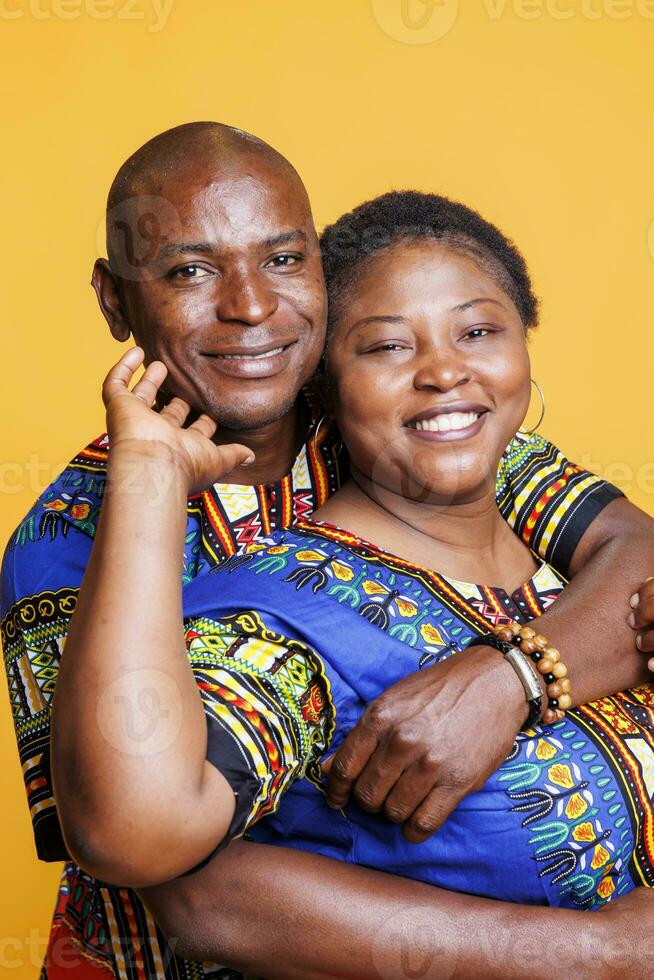 Smiling black couple in relationship embracing, showing love and happiness portrait. Joyful mature wife and husband romantic pair hugging and looking at camera with cheerful expression photo