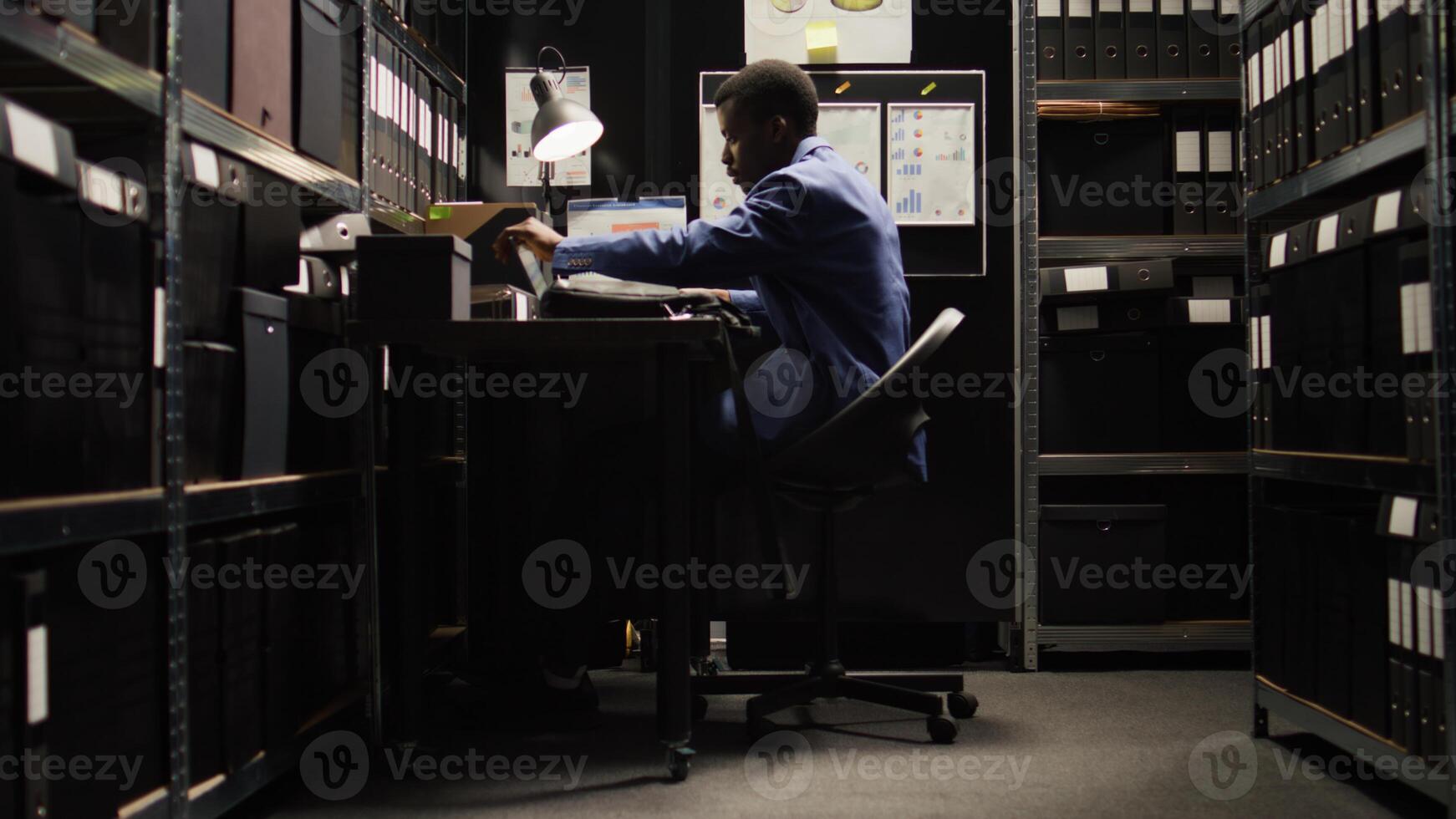 African American detective in archive room, reviewing evidence and files, with reliance on technology. Police officer conducts forensic investigation and background checks, ensuring justice shines. photo