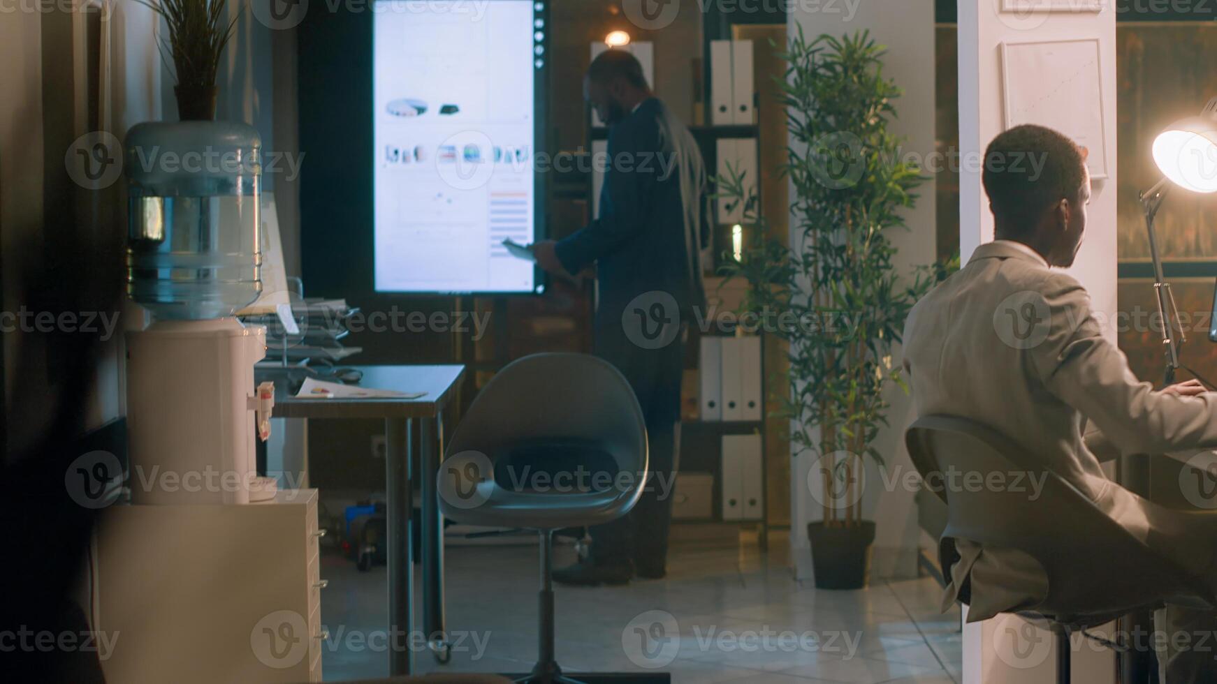 Employee enjoying cup of coffee while checking statistical graphs on computer during nightshift, helped by manager. Accountant working in office under management executive scrutiny photo