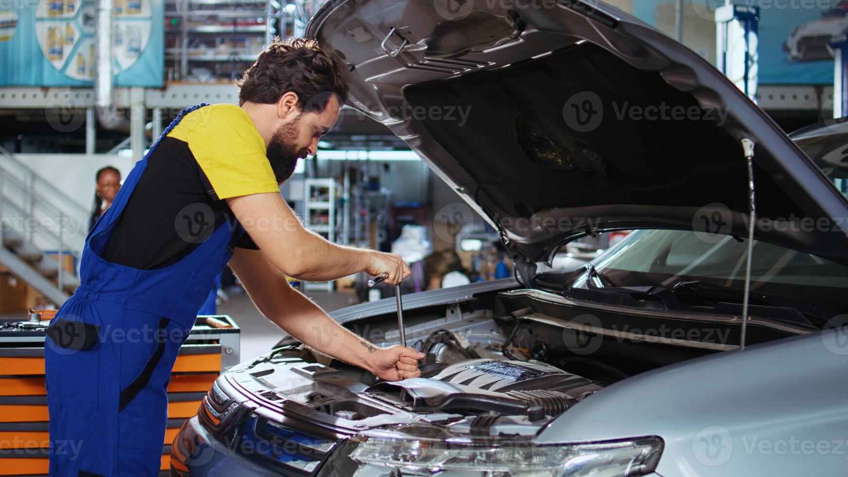 Trained technician in auto repair shop using virtual reality goggles to visualize car components in order to fix them. Man wearing modern vr headset while working on busted vehicle photo
