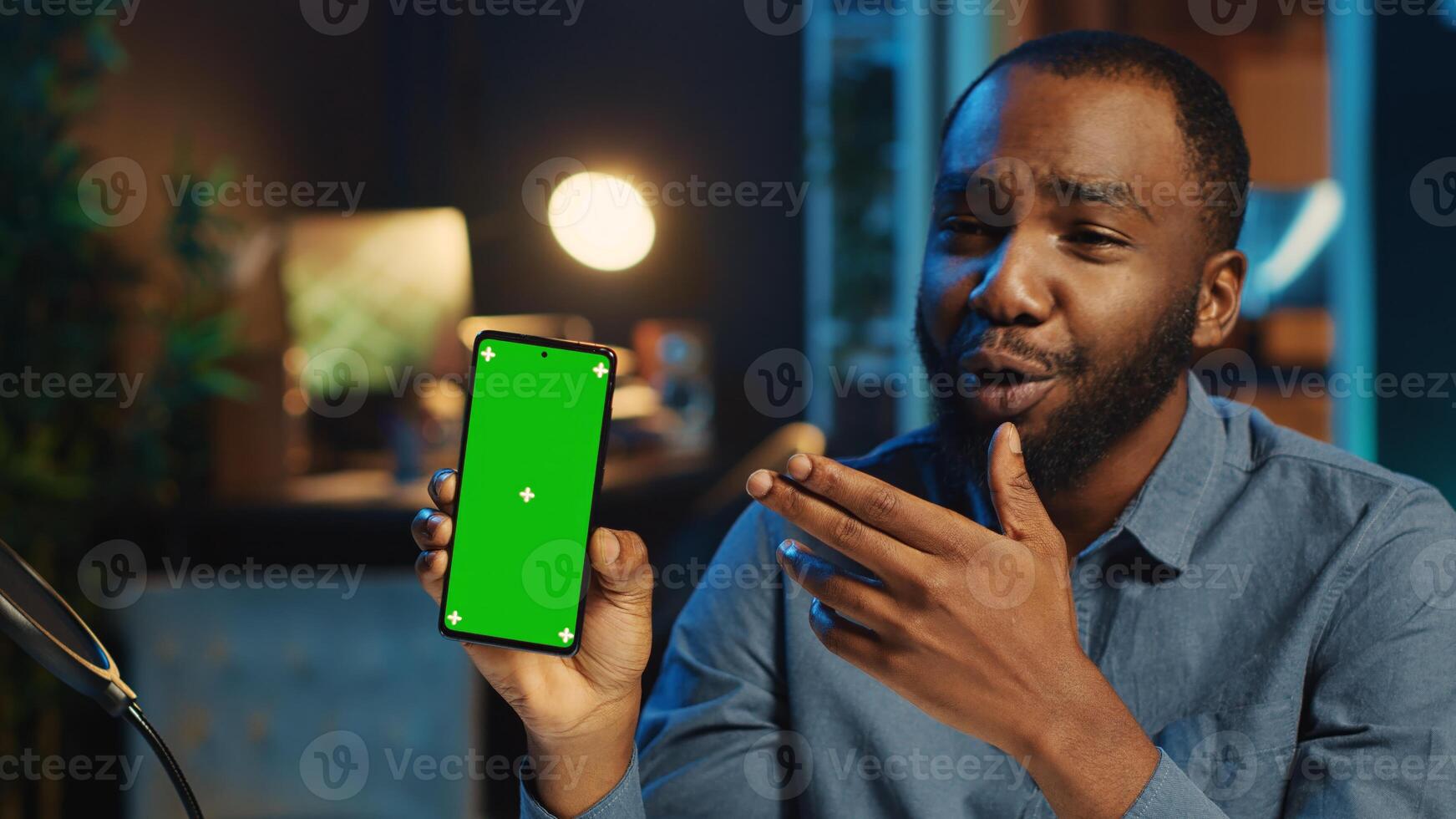 Smiling BIPOC content creator films mockup smartphone video review for tech enthusiasts. Trending media star hosts technology internet show, unboxing isolated screen cellphone photo