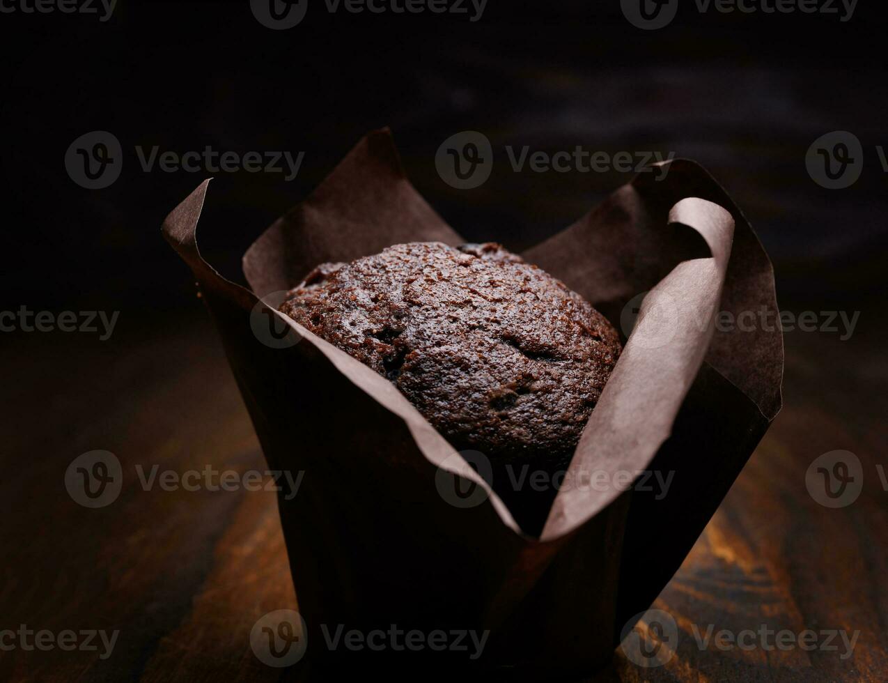 Chocolate cupcake on a dark background. Muffin with chocolate chips on a wooden surface. photo