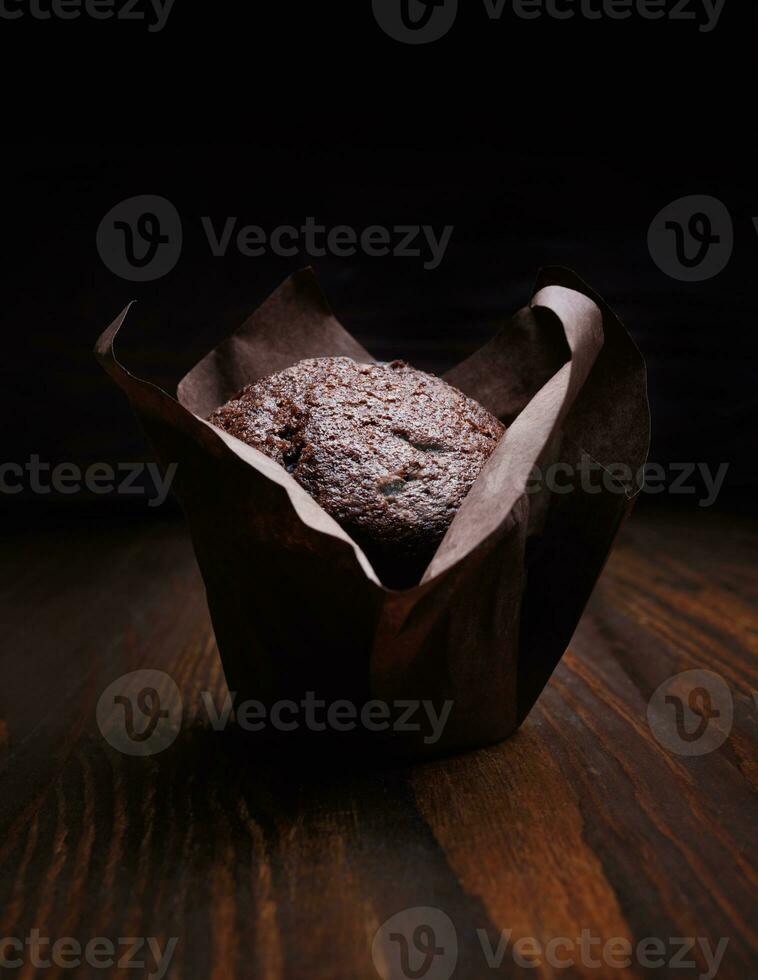 Chocolate cupcake on a dark background. Muffin with chocolate chips on a wooden surface. photo