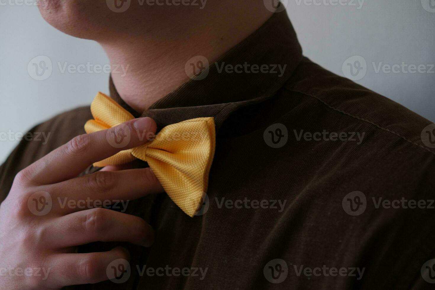 In the photo a man's white hand is holding a golden bow tie