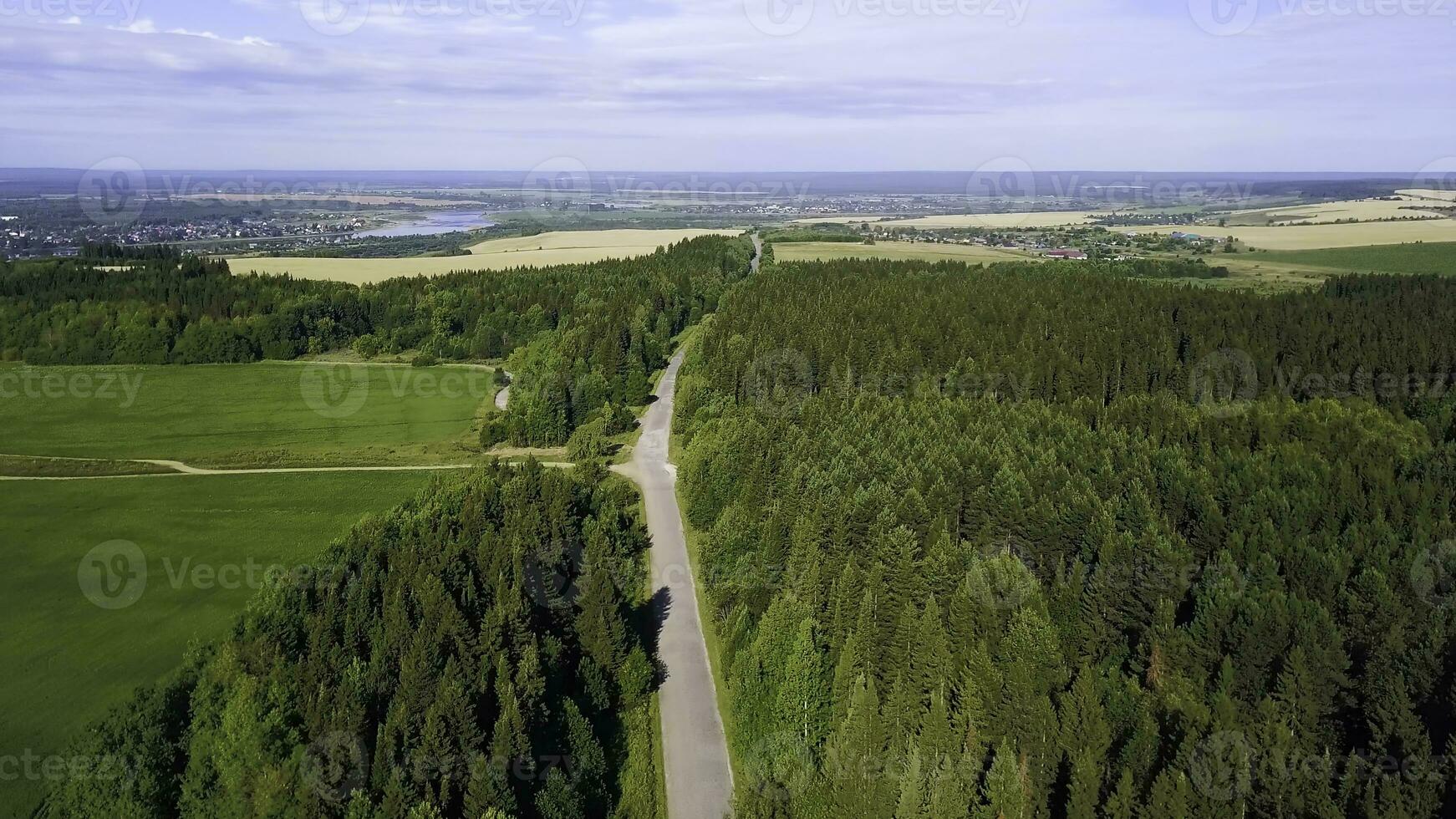 View from a helicopter. Creative. A summer green forest, a road, a small piece of the city is visible from behind, a blue sky and a river and a little small fields. photo