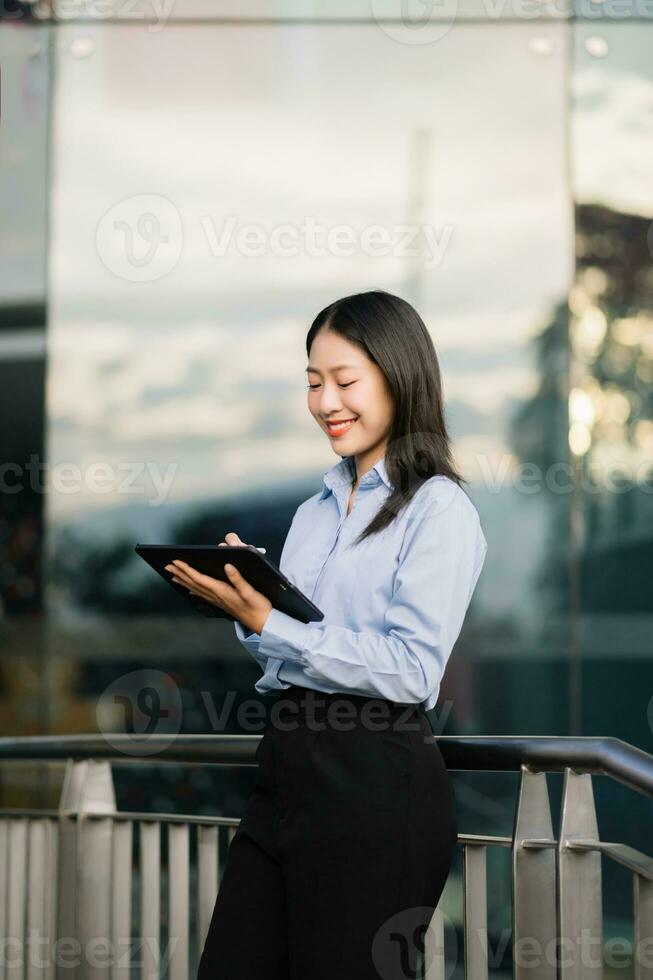 Young Asian business woman leader entrepreneur, professional manager holding digital tablet computer uon the street in big city photo