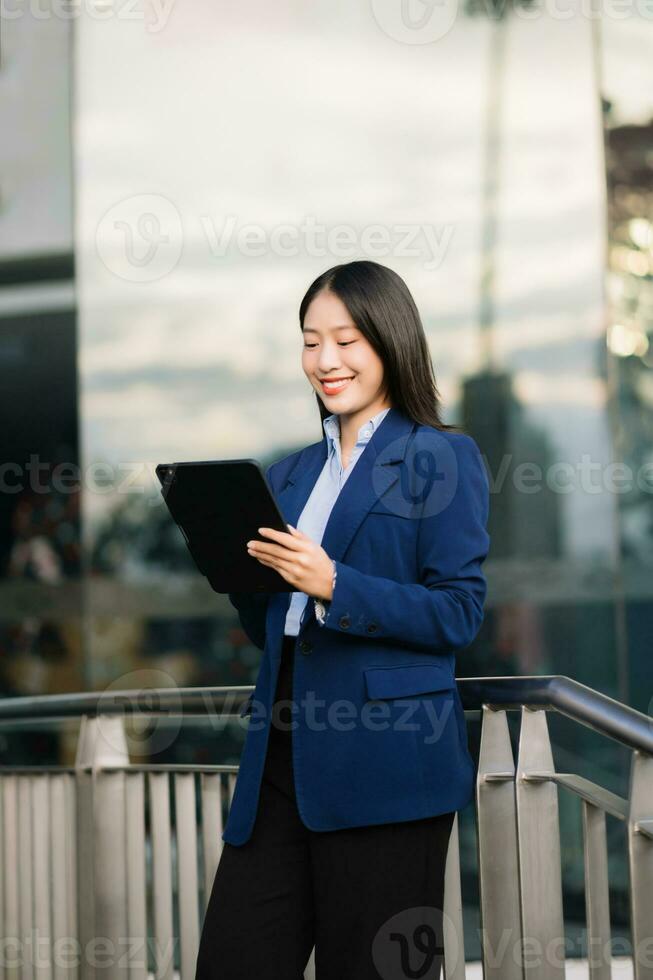 Young Asian business woman leader entrepreneur, professional manager holding digital tablet computer uon the street in big city photo