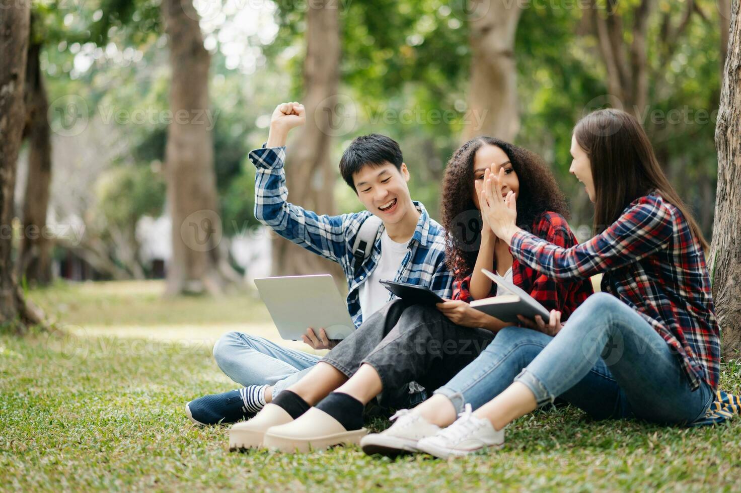 Three young college students is reading a book while relaxing sitting on grass in a campus park with her friends. Education concept photo