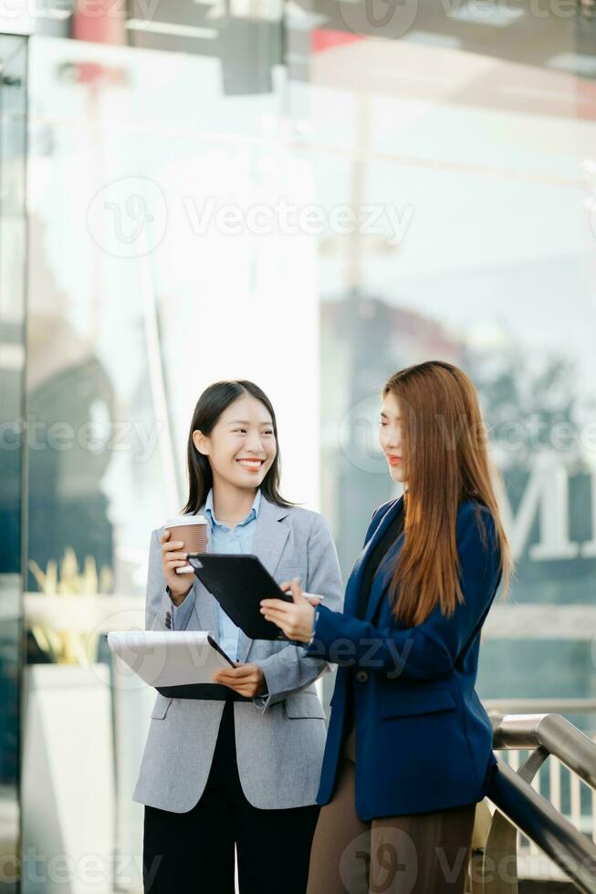 Businesswoman and woman going in city center in smart casual business style, talking, working together, stylish freelance people, holding tablet photo