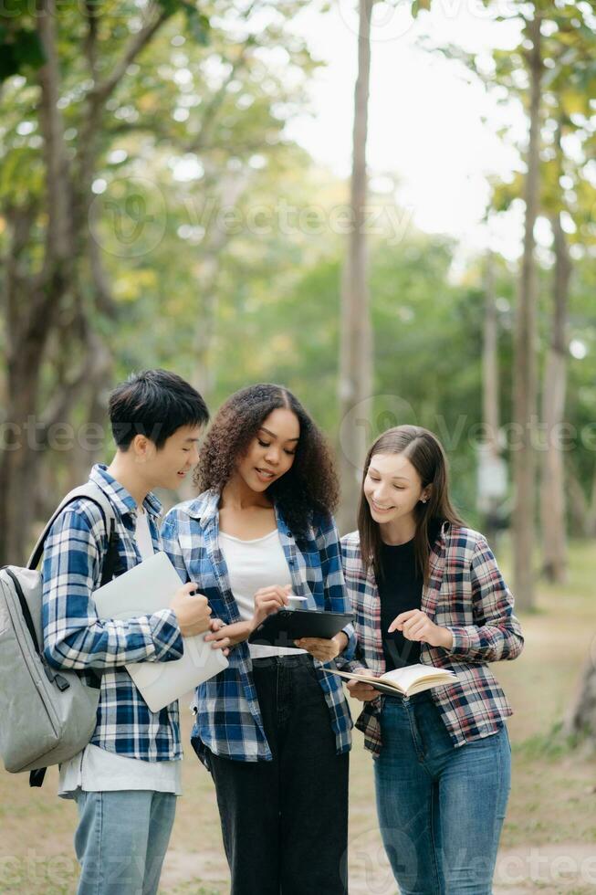 Three young college students is reading a book while relaxing sitting on grass in a campus park with her friends. Education concept photo