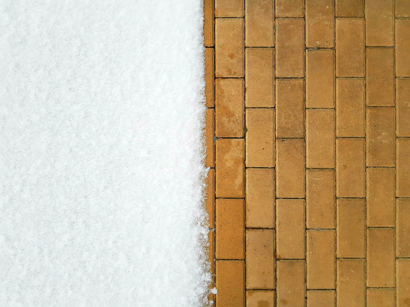 The left half of the yellow sidewalk is covered with white snow, a clear border. Pavement horizontal background. Place for your text here photo