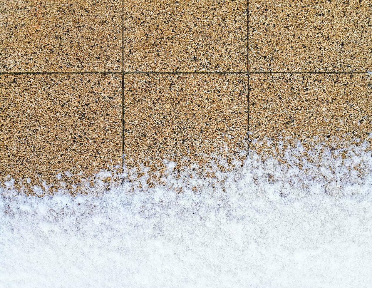 Sidewalk partially covered with snow at the bottom. Paving slabs made of very small pebbles, brown and beige. Pavement horizontal background. Place for your text here photo