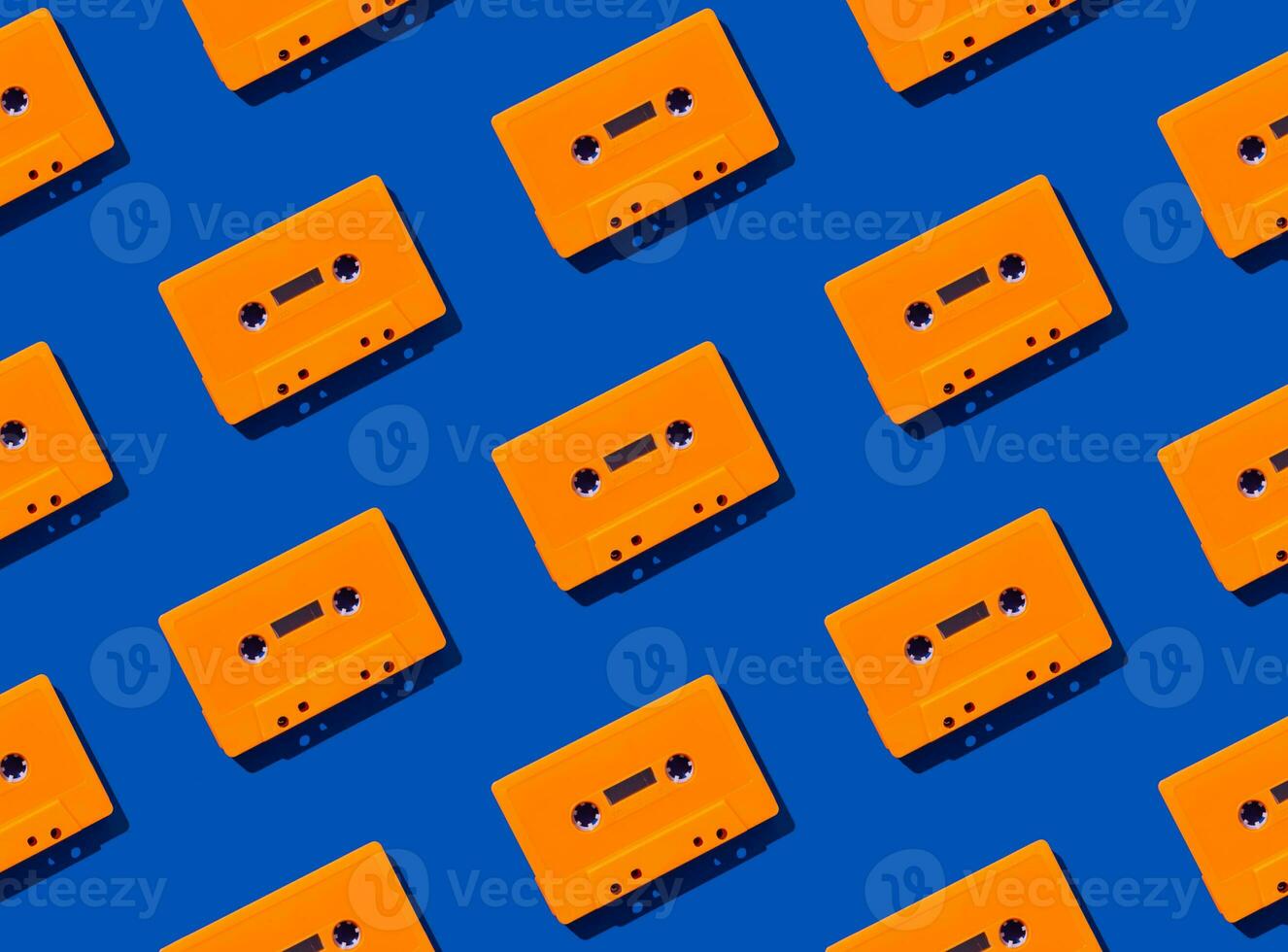 Pattern made with retro orange audio cassette tapes on blue background. Creative concept of retro technology. 80's aesthetic. Vintage audio cassette tape pattern idea. Retro nostalgia. Flat lay. photo