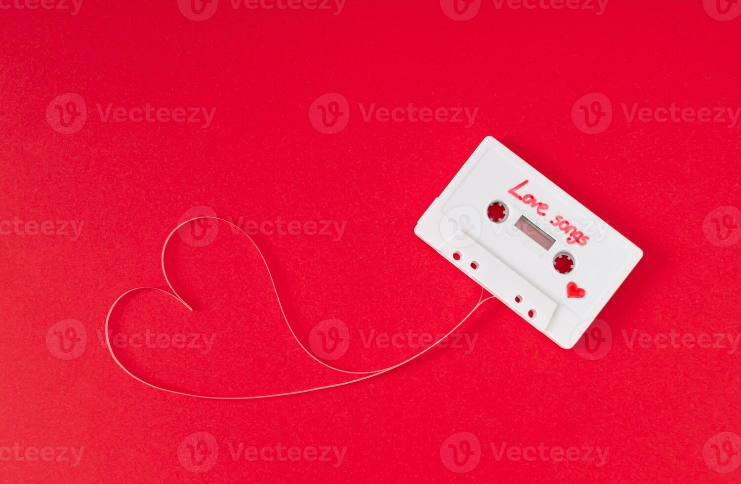 Audio cassette with loose tape shaping a heart on red background. Minimal love concept. Creative retro technology love card. 80's aesthetic. Vintage cassette tape love songs idea. Retro nostalgia. photo