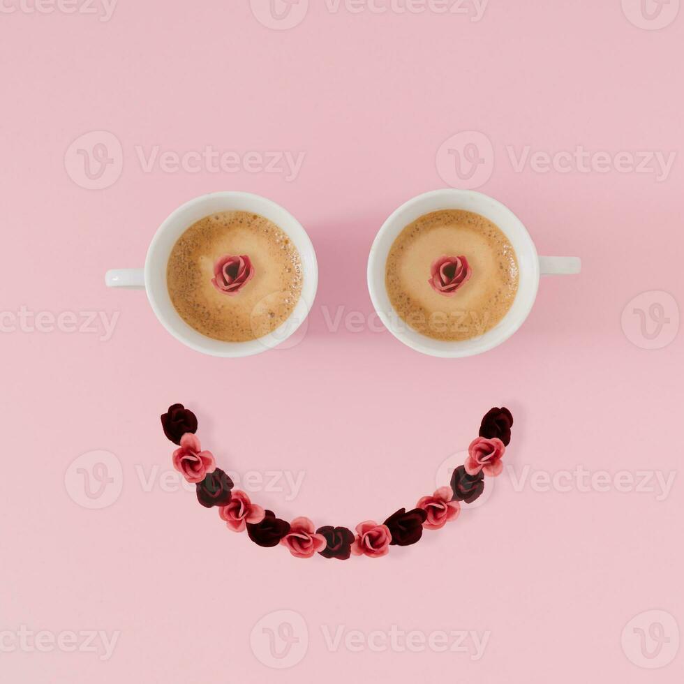 Layout of smiley emoticon made with coffee cups and flowers on pink background. Minimal coffee concept. Creative positive thinking and good mood idea. Coffee and flowers aesthetic. Flat lay. photo