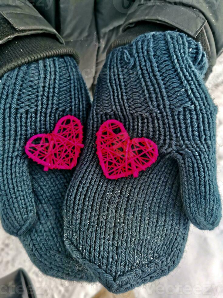 Close-up two hand-made of braided crimson colored hearts in men's hands dressed in winter blue knitted mittens photo