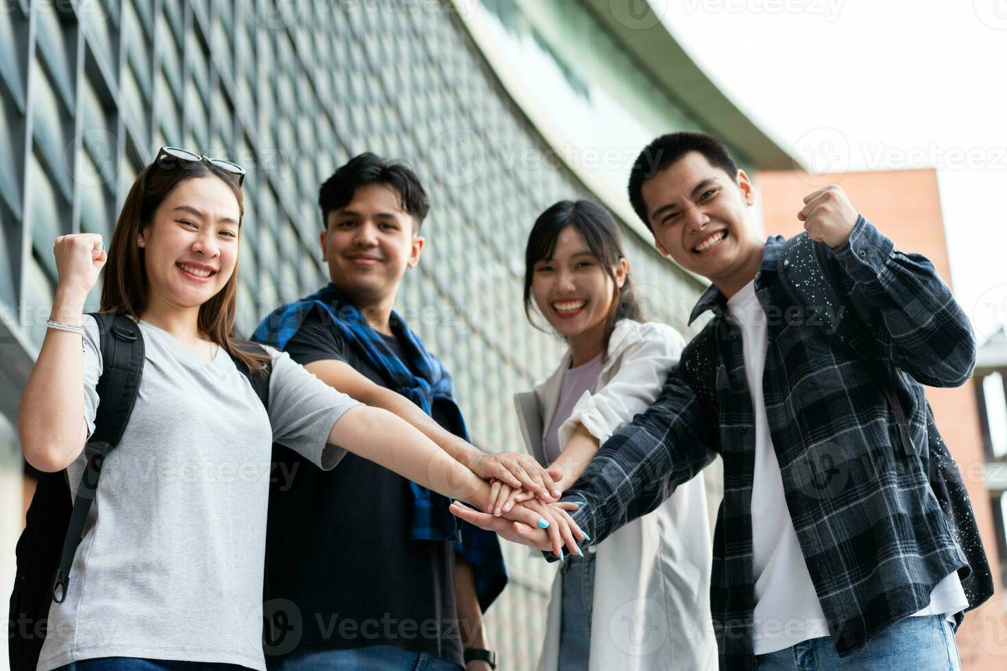 Group of cheerful young Asian entrepreneurs joining hands together to celebrate, excited success for achievements obtained. Undergraduate students celebrate success after end project, teamwork concept photo