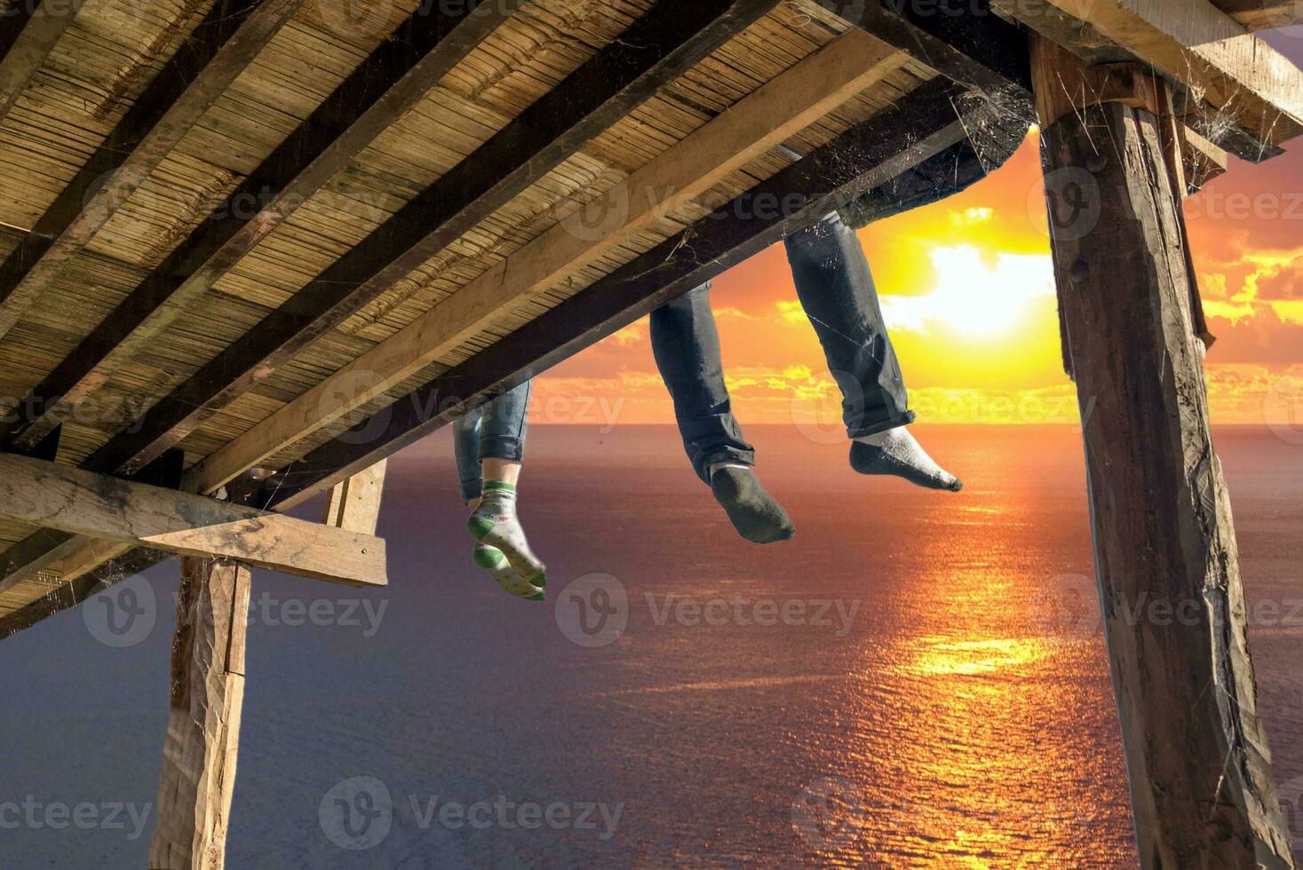 turistas sentado piernas colgando en de madera terraza disfrutar con Oceano a puesta de sol foto